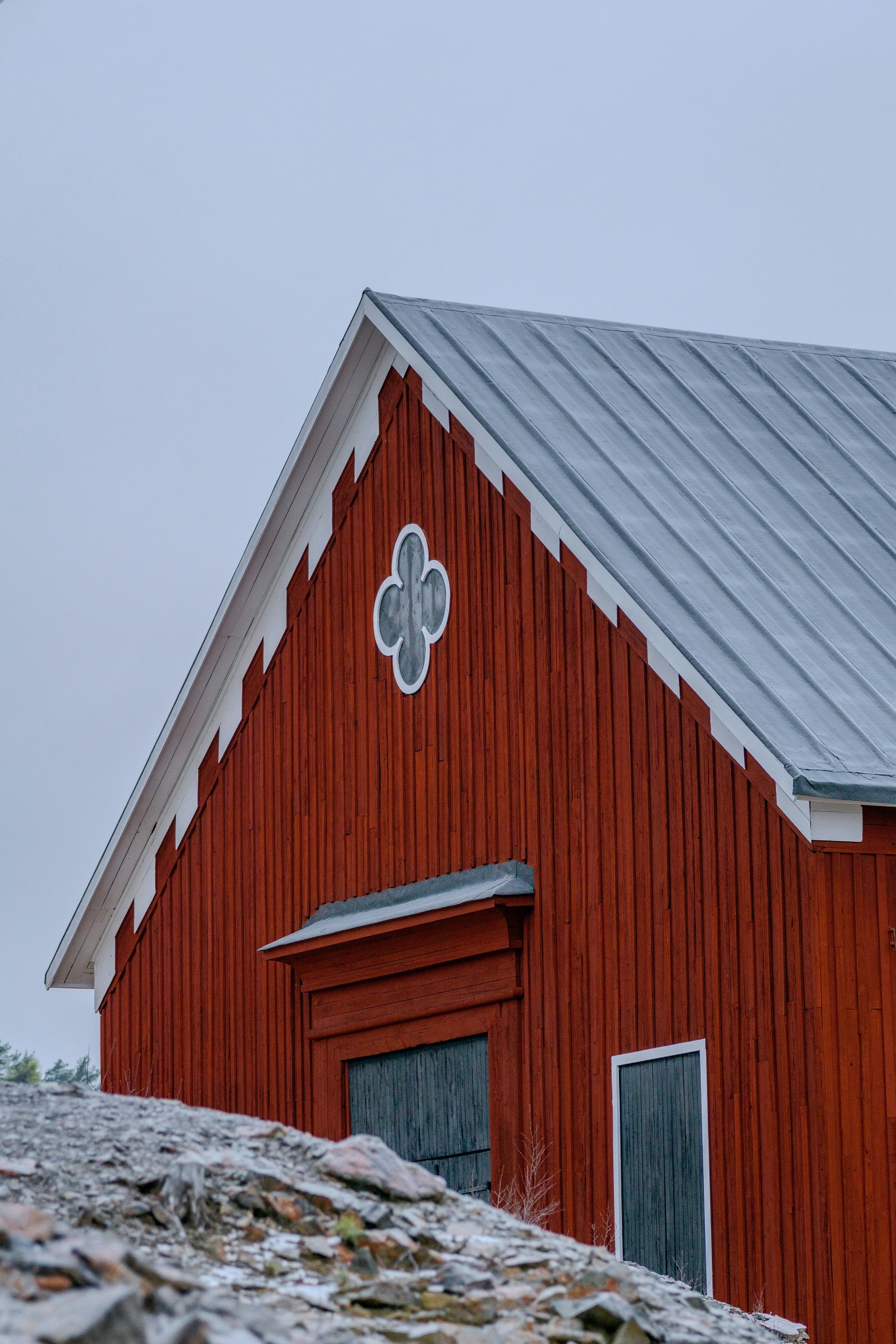 The gable of a Falu red timber building with a quatrefoil window, above a slag heap, Falun